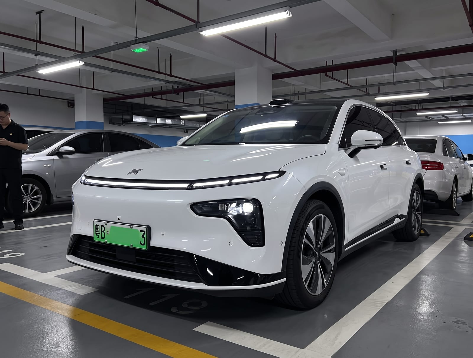 A white electric SUV with a green Chinese energy-vehicle license plate, parked in an underground garage