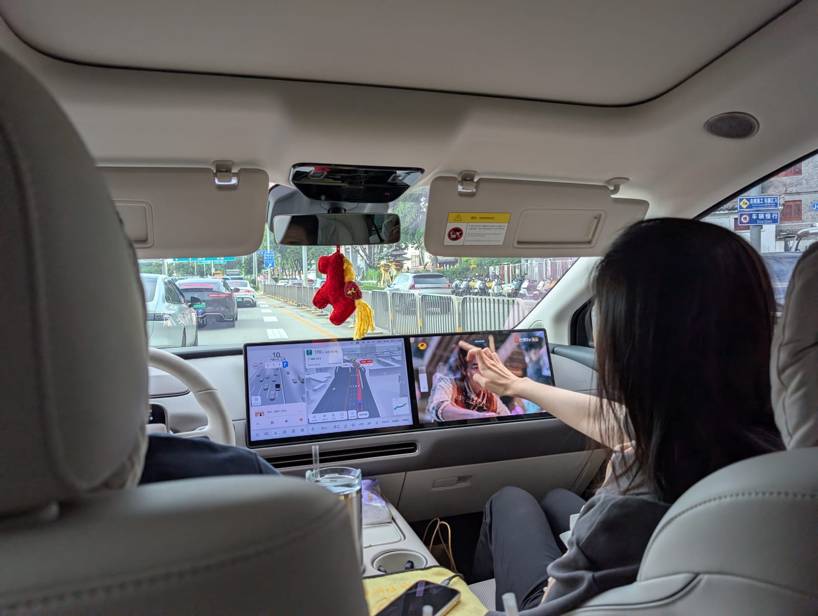 View from the back seat of the car, showing a navigation display for the driver and a separate entertainment screen for the front passenger
