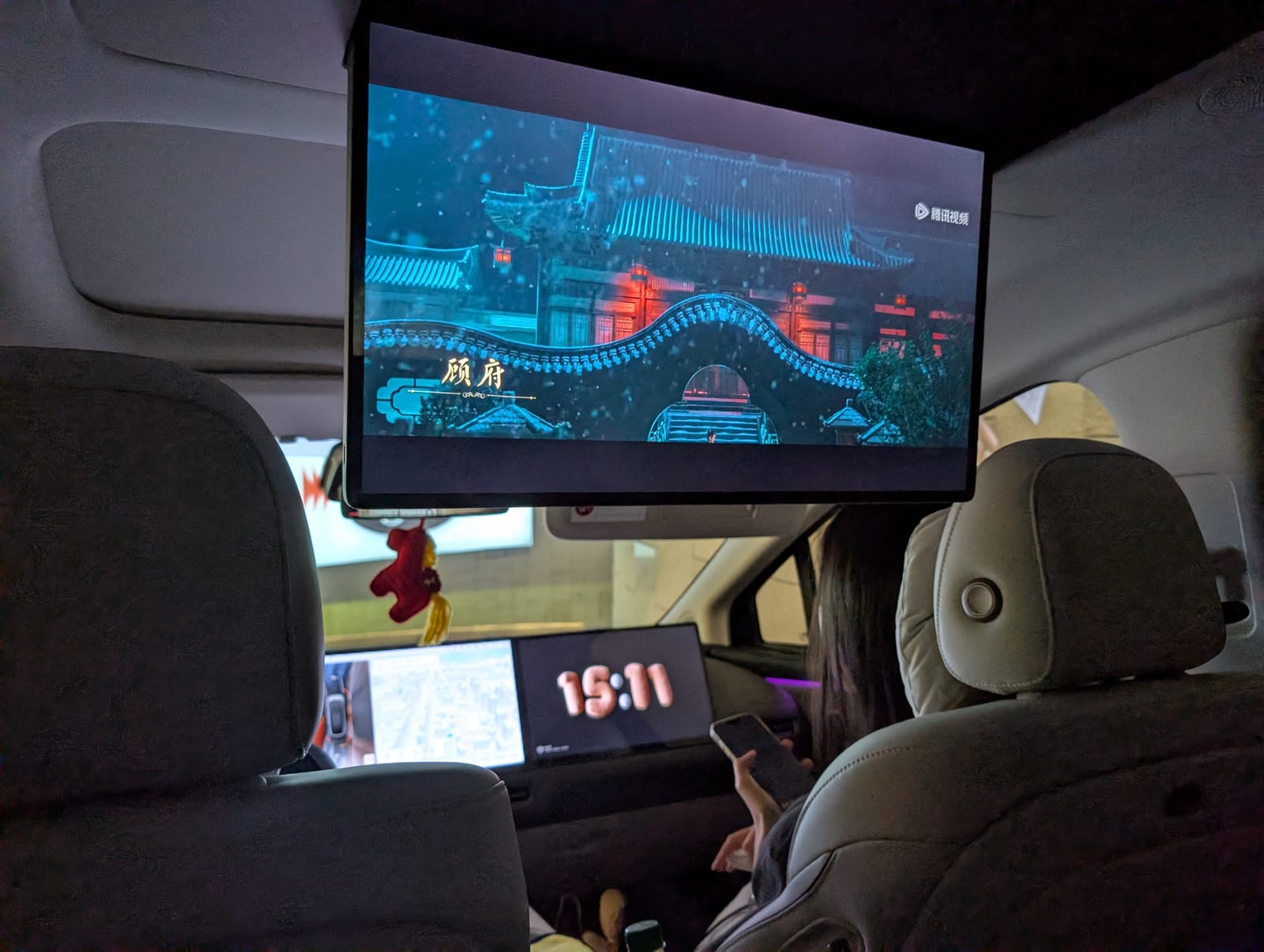 A large screen folded down from the ceiling of the car playing a Chinese period drama for rear-seat passengers