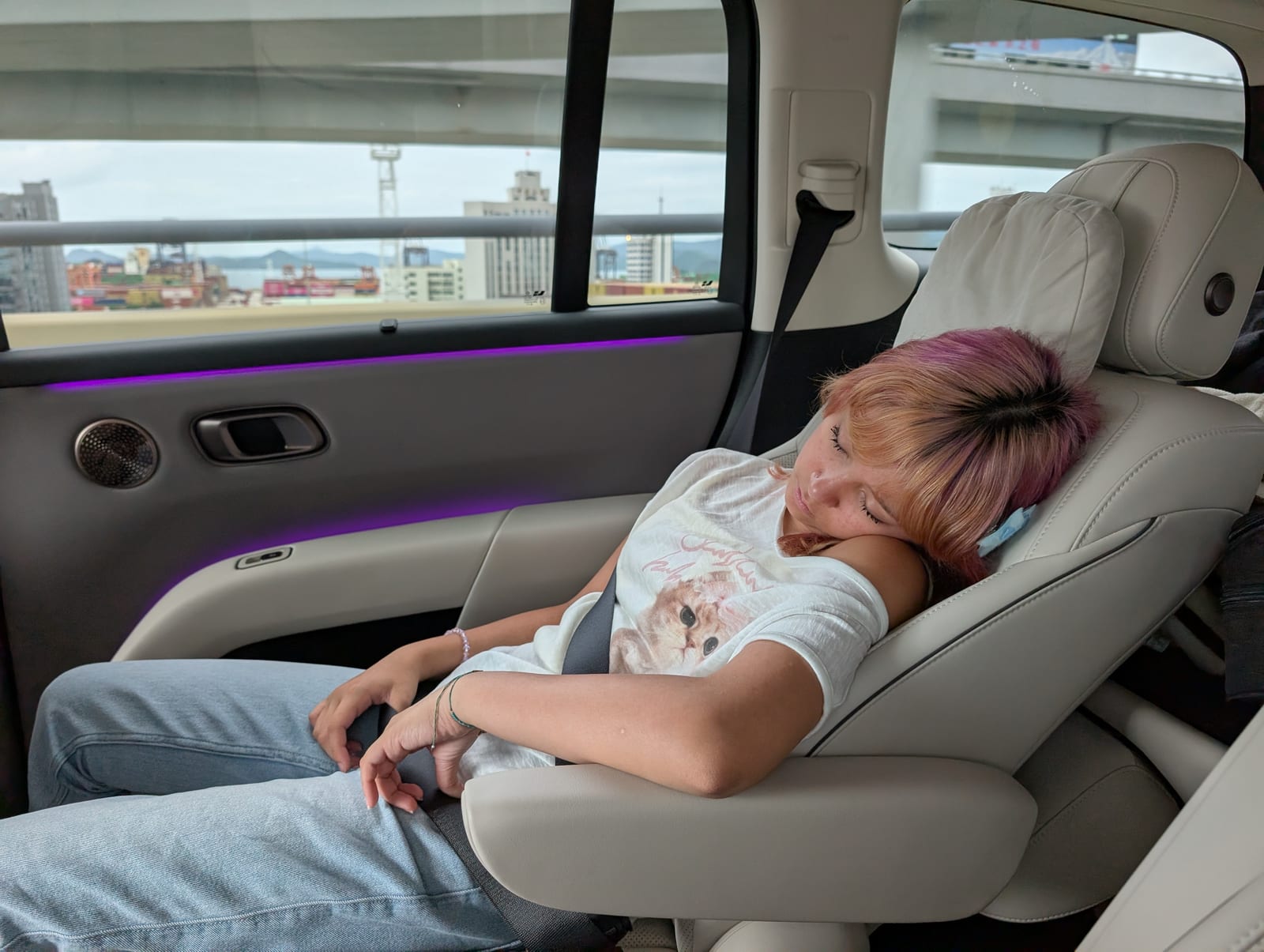 A reclined rear seat with a headrest pillow and purple ambient lighting along the door panel