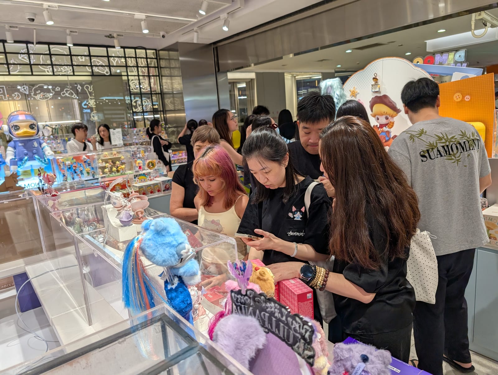 Shoppers of different ages gathered around display cases of collectible figurines in a busy Pop Mart store
