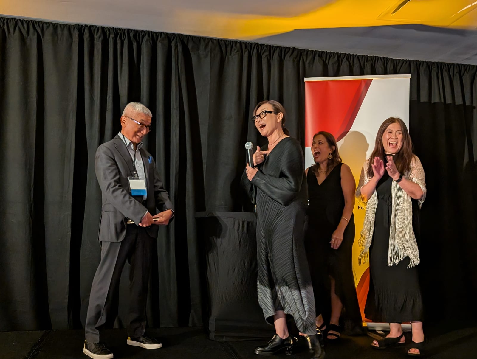 Bill Imada and Julia Huang on stage at the 3AF Fall Summit, laughing as Julia speaks into a microphone