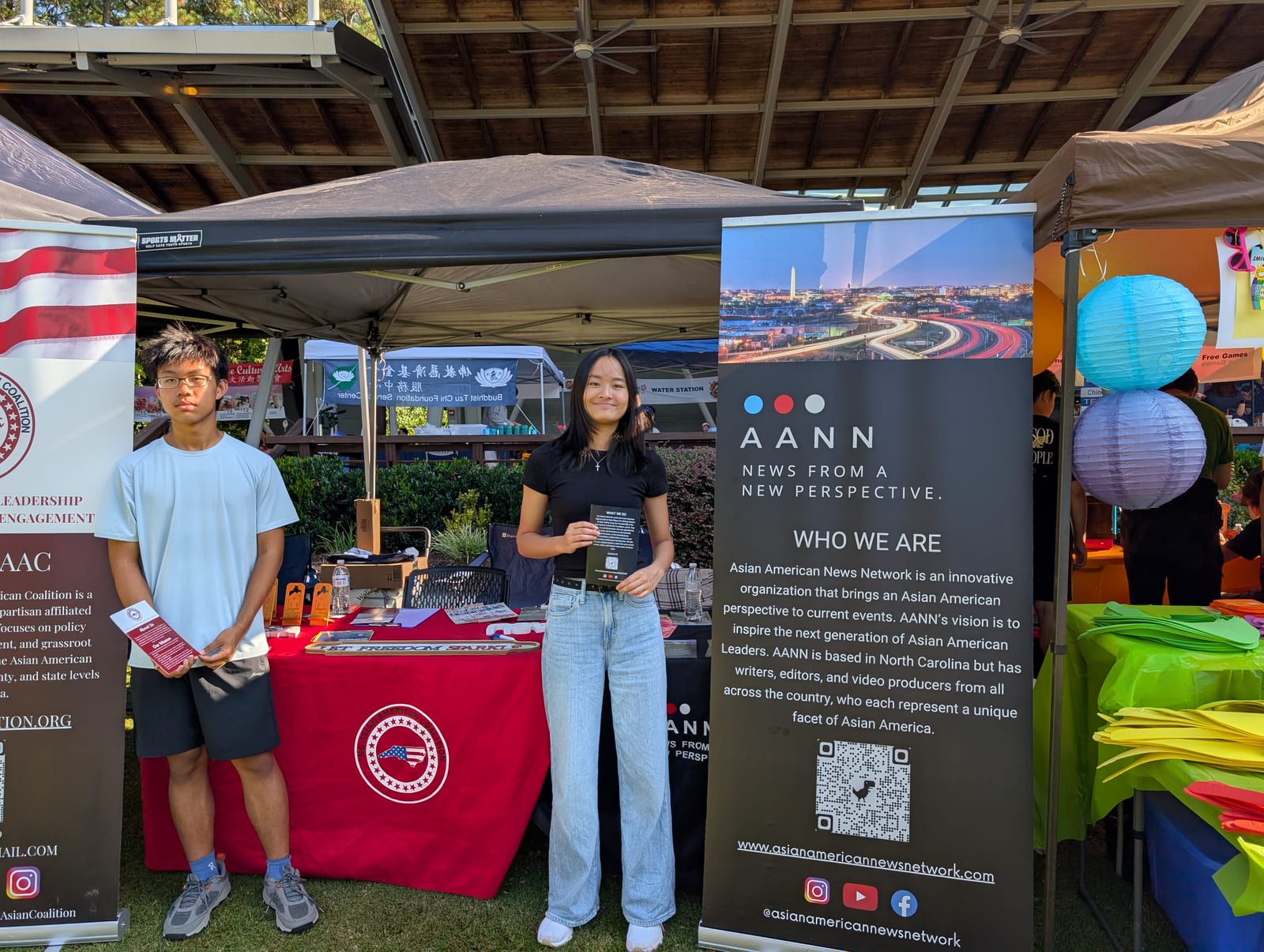 Two high-school students staffing the Asian American News Network booth, beside a banner reading News from a new perspective