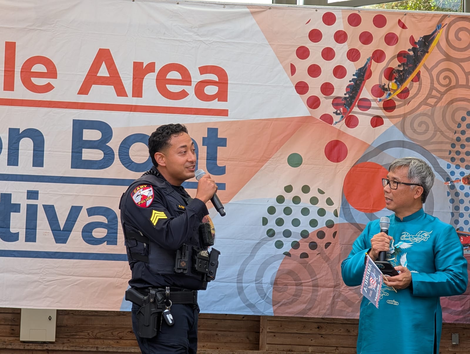 Sergeant Gilbert Candelaria of Cary speaking into a microphone beside Asian Focus board member Tho H. Nguyen at the festival stage
