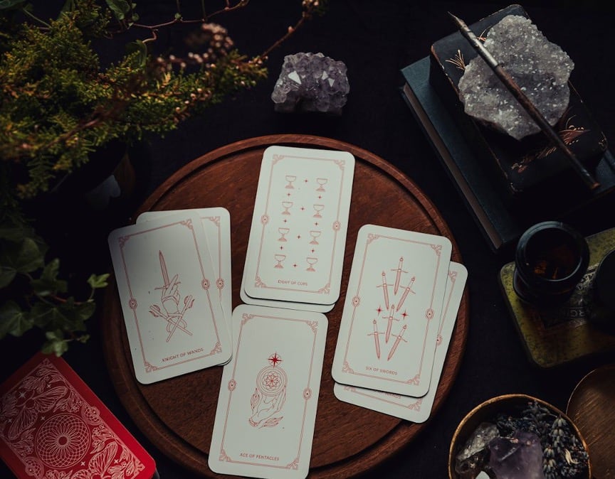 Tarot cards laid out on a wooden board beside amethyst crystals, dried flowers, and candlelight